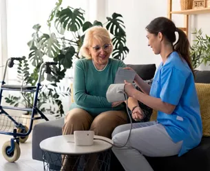 Caregiver holding older woman’s hand while sitting together on living room sofa