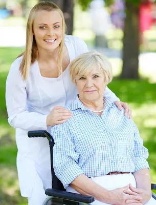 Caregiver assisting elderly woman with walking inside a bright living room